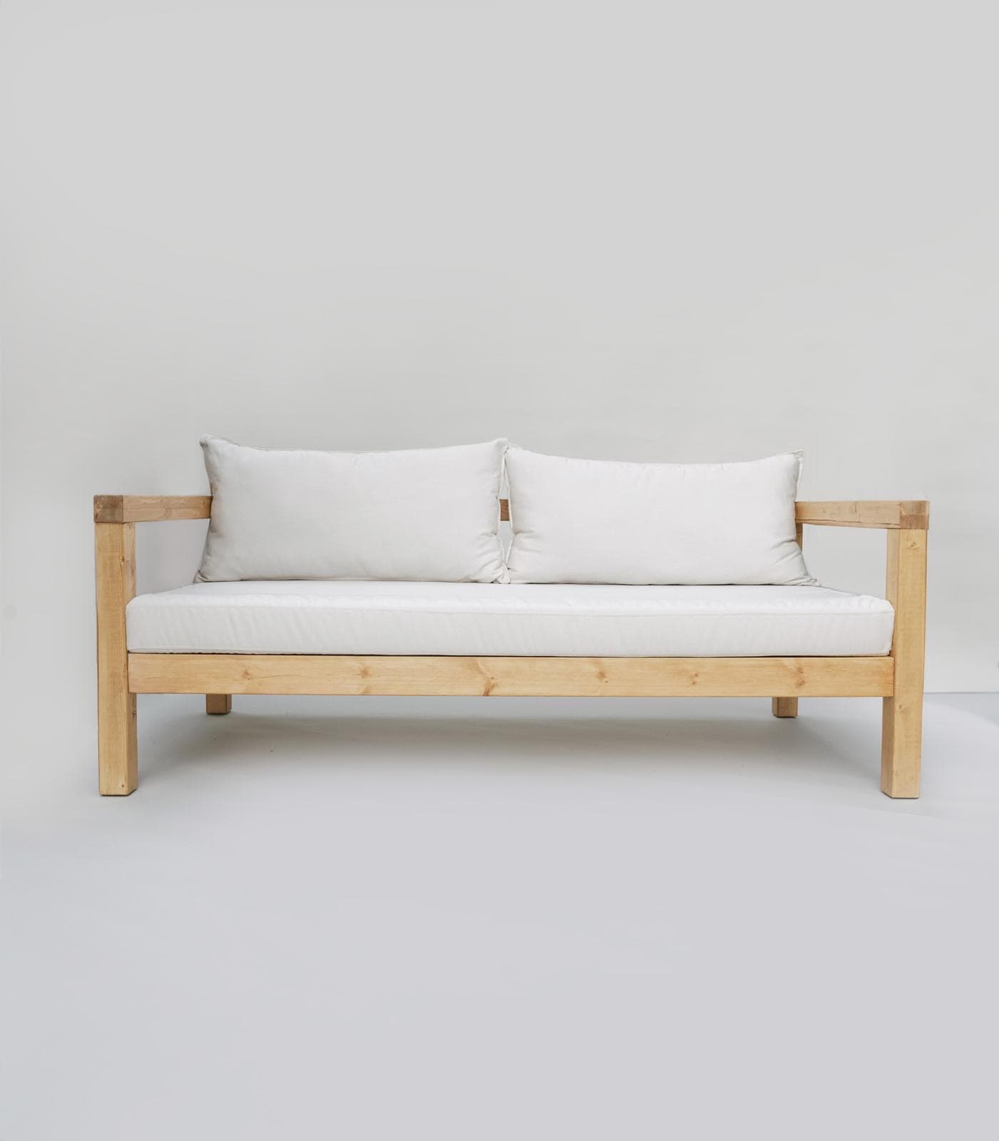 A modern, minimalist sofa with a wooden frame and white cushions. The sofa has a visible wooden structure, including the legs, armrests, and seat frame. It features two rectangular white seat cushions and two rectangular white back cushions. The cushions appear to be upholstered in a light-colored fabric and are slightly tufted. A small, discreet brown tag is visible on the right back cushion. The overall design is simple and rectilinear, suggesting it might be suitable for outdoor or indoor use. — 3D model