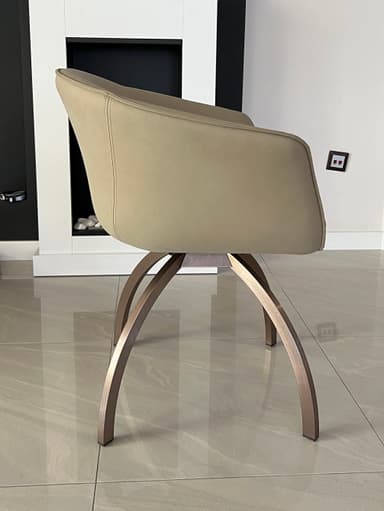 A modern accent chair with a curved, upholstered back and seat. The chair is supported by a distinctive base composed of four curved legs that splay outwards, made of a metallic material. A vertical seam with a zipper-like detail runs up the center of the chair's back. — 3D model