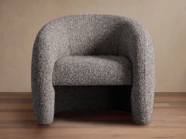 A generously proportioned armchair with a rounded, enveloping silhouette. The chair features a fully upholstered form with a high back that curves around to form integrated armrests. The upholstery has a textured, boucle-like appearance, creating a soft and inviting aesthetic. The base appears to be a continuous, rounded structure that extends to the floor, without visible legs. — 3D model