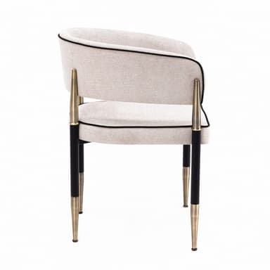 A contemporary upholstered armchair featuring a curved barrel back and seat, covered in a light beige textured fabric with distinct black piping. The chair is supported by a black metal frame with elegant brass accents on the integrated armrests and tapered leg tips. — 3D model