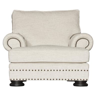 A single armchair upholstered in a textured light-colored fabric. It features rolled arms adorned with decorative nailhead trim, a plush seat cushion, and a supportive back cushion. The base of the chair is also upholstered and features a double row of nailhead trim, supported by four dark wooden bun feet. — 3D model