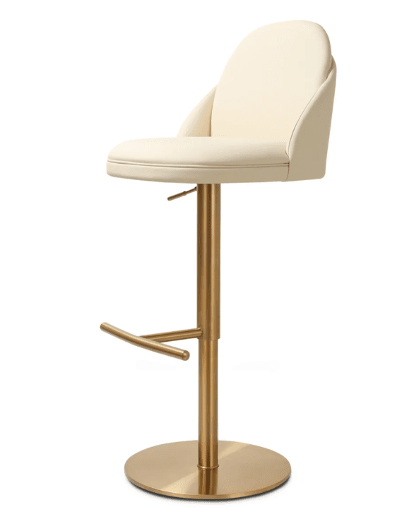 A modern bar stool featuring a cream-colored upholstered seat and backrest, mounted on a brushed brass-finished metallic base. The seat has a rounded, gently curved backrest, offering partial arm support. The central column is height-adjustable via a lever located beneath the seat. A circular footrest extends from the column, and the stool rests on a flat, circular base. — 3D model