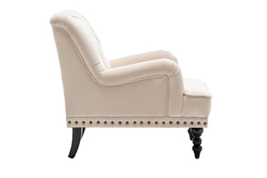 A traditional upholstered armchair featuring a light cream fabric, rolled armrests, a tufted backrest, and decorative nailhead trim along the base. The chair stands on dark-finished legs, with turned spool-shaped legs at the front and tapered saber legs at the rear. — 3D model