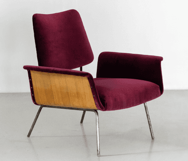 A modern armchair with a distinct mid-century aesthetic. It features a curved backrest and seat upholstered in a deep burgundy, possibly velvet or a similar textured fabric. The armrests are integrated into the main body of the chair. A prominent design element is the exposed wooden panel on the sides, appearing to be bent plywood, which contrasts with the upholstered sections. The chair is supported by slender, metallic legs that angle outwards. — 3D model