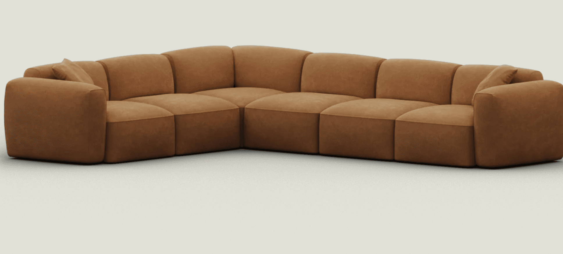 An L-shaped, modular sectional sofa upholstered in a warm camel brown microsuede-like fabric. The sofa features a soft, rounded profile with plush, integrated seat and back cushions. It consists of multiple segments, including corner and armrest pieces, creating a cohesive, inviting seating arrangement. The design is low-slung and minimalist, emphasizing comfort. — 3D model