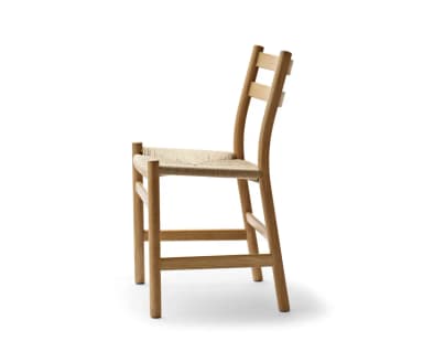 A minimalist dining chair crafted from natural oak wood, featuring an armless design with a gently curved, two-slat ladder backrest. The seat is hand-woven with natural paper cord, creating a textural contrast with the smooth wood frame. The chair stands on four round, tapered legs, with stretchers providing stability. — 3D model