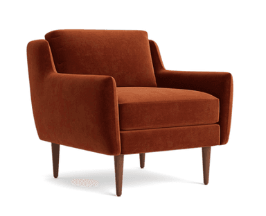 A contemporary armchair upholstered in a rich burnt orange velvet fabric. It features a boxy silhouette with slightly angled, wide arms that flow into the backrest. The armchair has a loose seat cushion and a separate back cushion, both generously padded. It stands on four slender, tapered wooden legs with a medium-dark finish. The design suggests a blend of modern and mid-century aesthetics. — 3D model