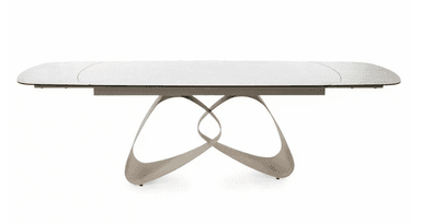 A modern dining table with a rectangular, elongated tabletop featuring softly rounded corners. The tabletop has a subtle texture and appears to be a light, neutral color, possibly white or light gray. It is supported by a sculptural base composed of interlocking, fluid shapes that create an abstract, organic form. The base has a metallic or polished finish, reflecting light and adding a dynamic visual element. The overall design suggests contemporary aesthetics. — 3D model