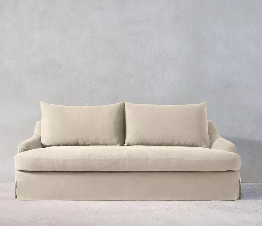 A upholstered sofa with a slipcover design. It features a plush seat and back cushions, with two rectangular throw pillows placed against the back. The sofa has a skirted base extending to the floor. — 3D model