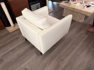A modern white sofa with a tufted backrest and armrests, upholstered in a material that appears to be faux leather or high-quality vinyl. It features a clean, minimalist design with slim, black metal legs. The stitching detail is visible along the edges. — 3D model