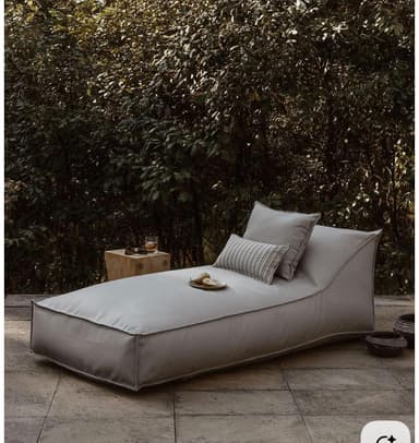 A contemporary grey fabric chaise lounge daybed with a low profile and two accompanying throw pillows, featuring visible piping along its edges. — 3D model