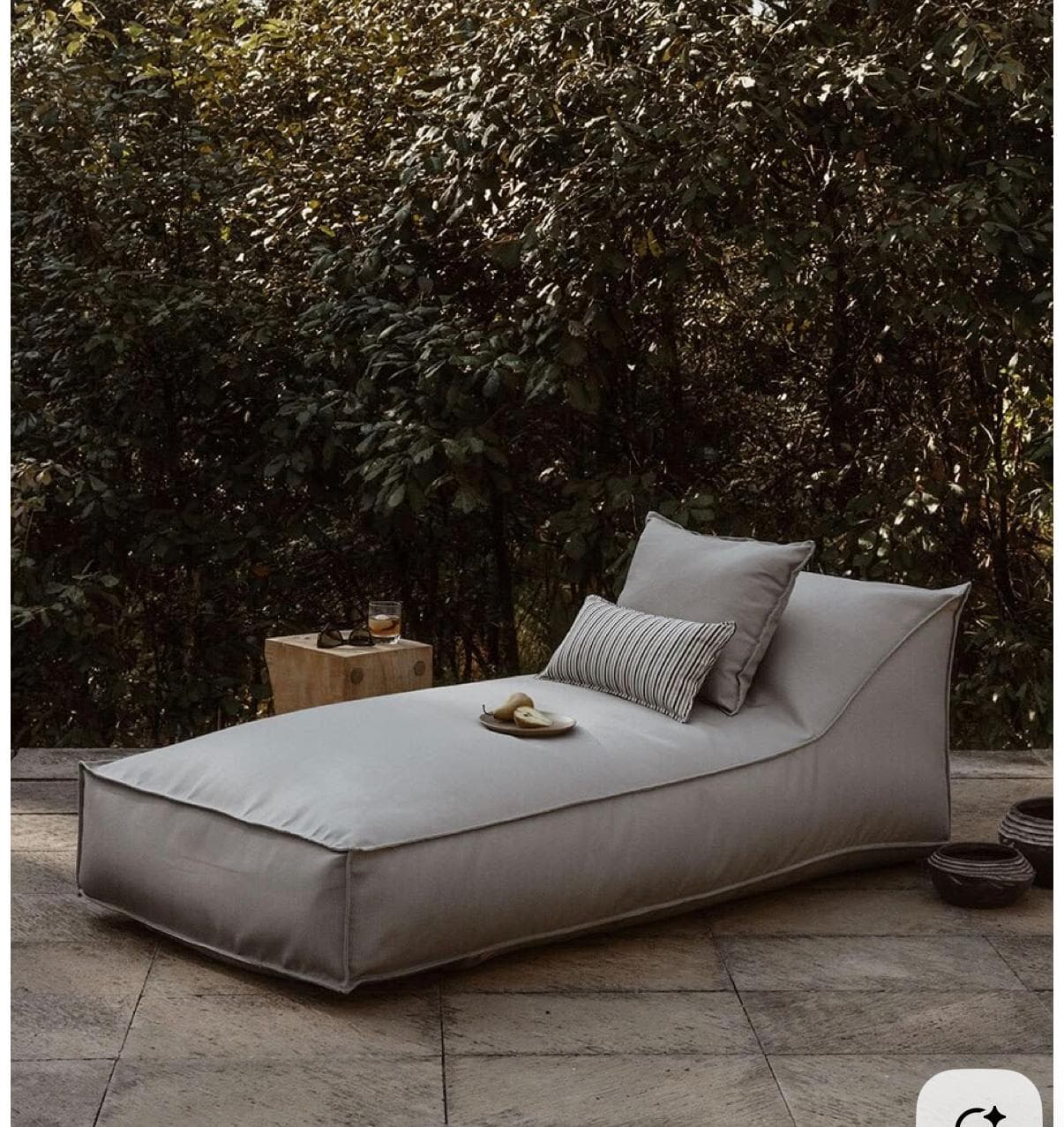 A contemporary grey fabric chaise lounge daybed with a low profile and two accompanying throw pillows, featuring visible piping along its edges. — 3D model