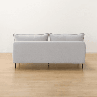 A contemporary armless chaise loveseat, upholstered in a light gray textured fabric. It features a low-profile design with a deep, elongated seat on the right side, resembling a chaise. The seating is supported by minimalist black metal legs, and the piece includes two large back cushions and two smaller rectangular throw pillows, all with subtle piped edges. — 3D model