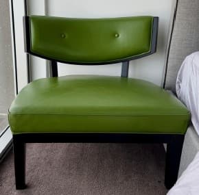 An armless accent chair featuring a low-profile design with a padded seat and a gently curved backrest, upholstered in a vibrant green faux leather. The chair is supported by a dark, possibly black, wooden frame and sturdy tapered legs. The backrest has two subtle button tufts. — 3D model