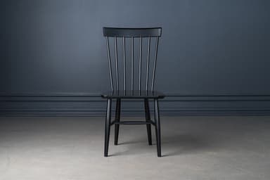 A classic black lacquered Windsor-style dining chair, featuring a tall spindle backrest and a solid wood saddle-shaped seat. The chair stands on four splayed and tapered legs, reinforced by H-stretchers, offering a timeless and sturdy design. — 3D model