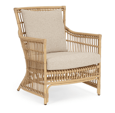 A light brown natural rattan lounge armchair featuring a curved, open-weave frame. It is fitted with thick, removable, light beige upholstered seat and back cushions. The chair has a rounded back and arms, with vertical rattan slats forming the back and side panels. The legs are integrated into the curved frame, with the rear legs slightly flared. The overall aesthetic is natural and relaxed. — 3D model