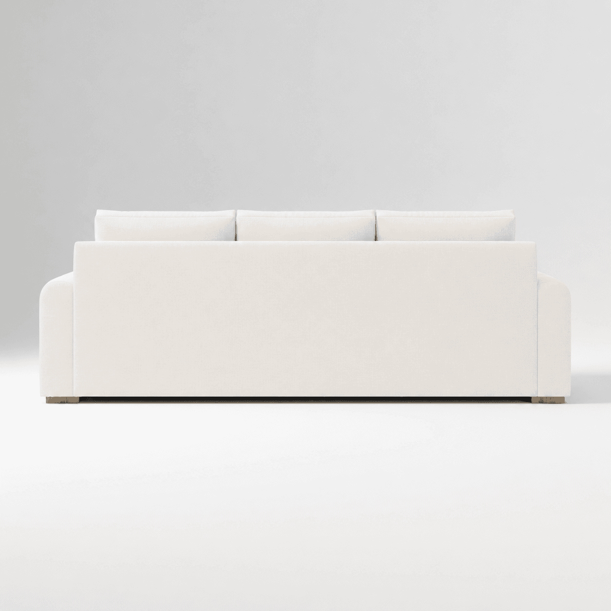 A contemporary three-seater sofa, viewed from the rear, featuring three loose back cushions and a low-profile base. The sofa is upholstered in a light-colored, possibly off-white or cream, textured fabric. The arms appear gently rounded on the outer edges. Small, recessed wooden feet are visible at the base corners. — 3D model