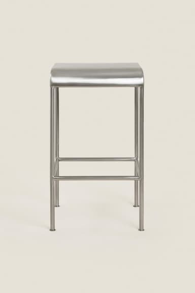 A minimalist, rectangular stool constructed entirely from brushed metal, featuring a seat with gently rounded corners and a tubular frame with integrated horizontal support bars. — 3D model
