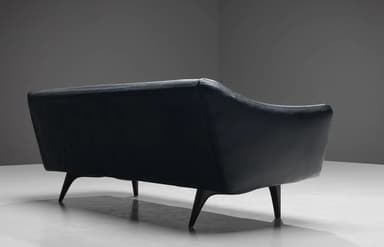 A three-seater sofa with a curved backrest and armrests, upholstered in dark leather. The seat is composed of three distinct cushions. The sofa is supported by four tapered wooden legs. — 3D model