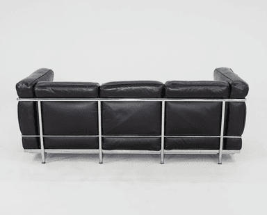 A three-seater sofa characterized by its boxy, geometric silhouette and exposed tubular chrome-plated steel frame. It features black leather upholstery on separate, plump cushions for the seat, back, and arms. The cushions appear to be removable and are designed to sit within the sturdy metal structure. The leather shows signs of use, such as creasing, indicating a well-loved piece. — 3D model