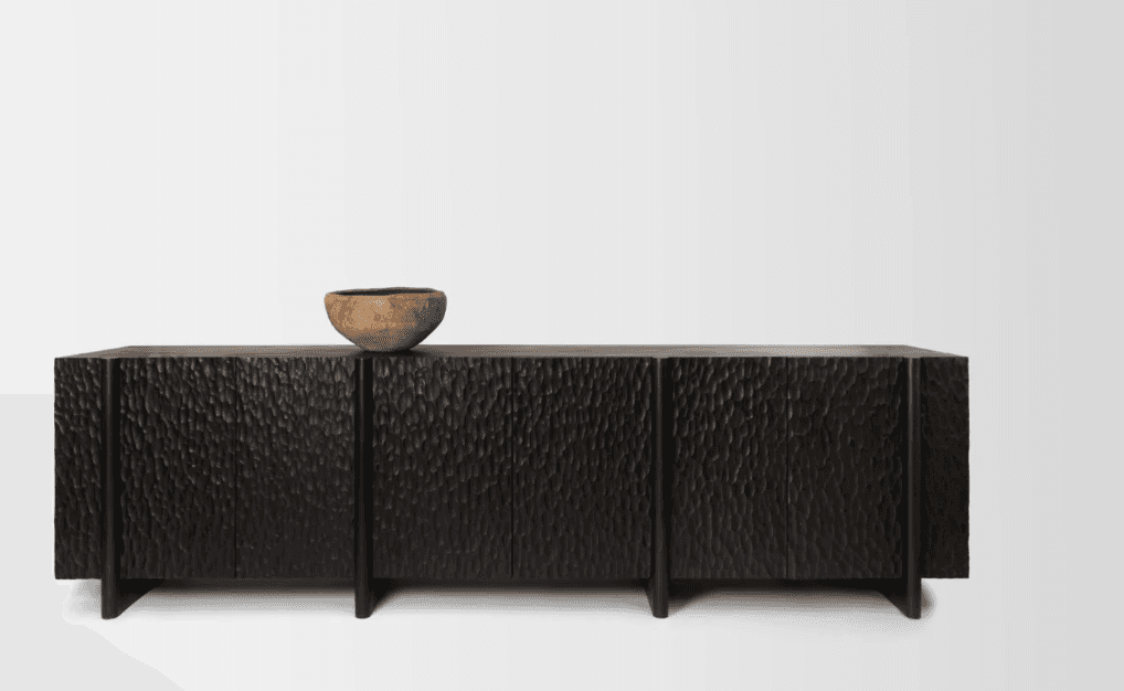 A dark-colored credenza with a textured front featuring multiple doors. The credenza has a rectangular top and stands on four legs. A rustic wooden bowl is placed on the top surface towards the left side. — 3D model