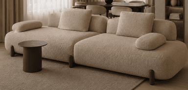 A modern modular sectional sofa upholstered in light beige boucle fabric, featuring soft, rounded edges and minimalist dark wooden legs. It consists of two distinct units, configured to create an L-shape, and includes loose back cushions and integrated bolster pillows. — 3D model