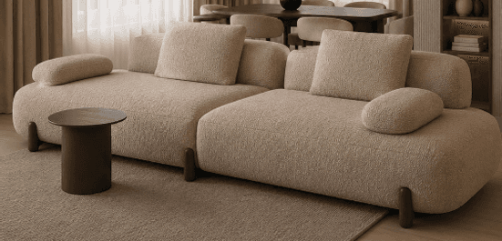 A modern modular sectional sofa upholstered in light beige boucle fabric, featuring soft, rounded edges and minimalist dark wooden legs. It consists of two distinct units, configured to create an L-shape, and includes loose back cushions and integrated bolster pillows. — 3D model