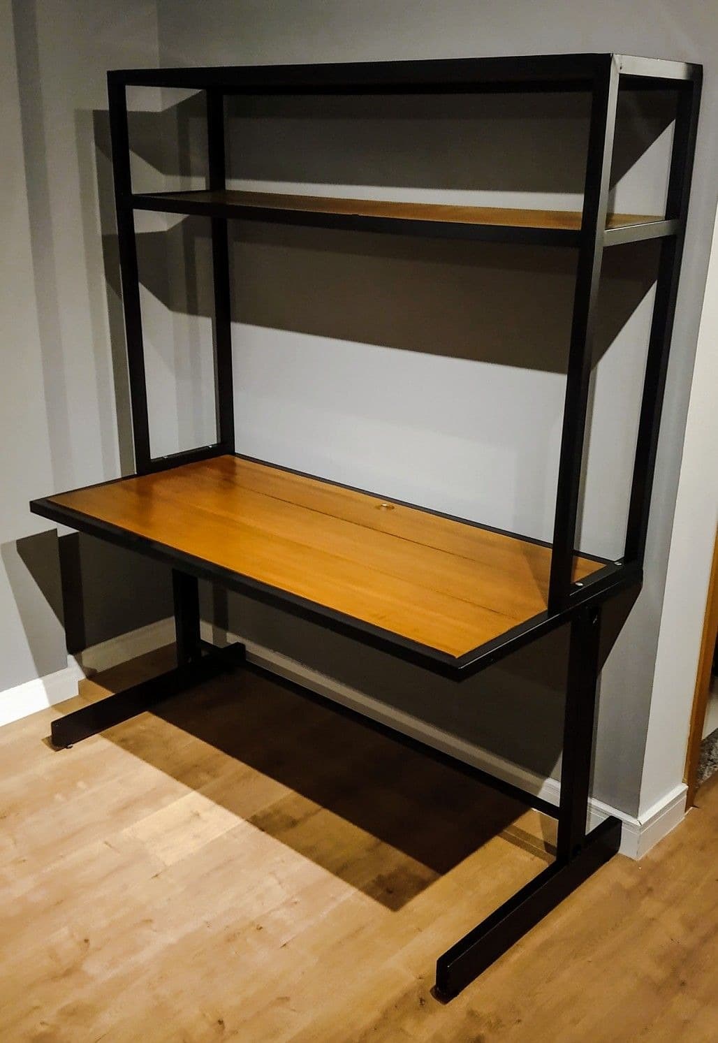 A contemporary desk unit featuring a black metal frame and wood-look laminate surfaces, incorporating a main rectangular desk surface and an integrated two-tier shelving hutch above. The design is minimalist and industrial-inspired, suitable for various modern office or home settings. — 3D model