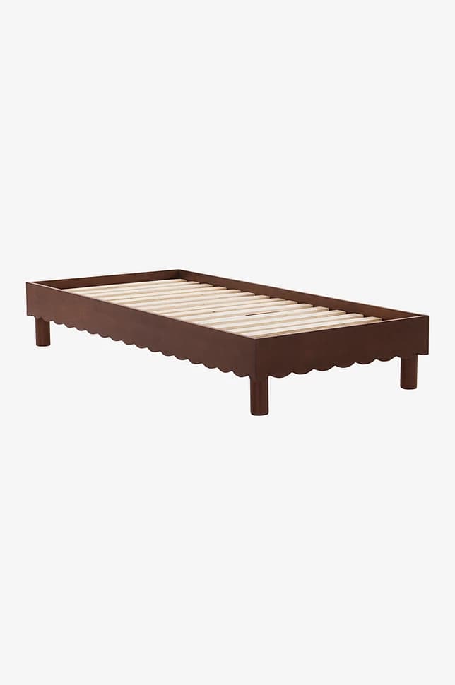 A bed frame with a scalloped edge along the side rails and four cylindrical legs. The frame supports a slatted mattress base made of light-colored wood. — 3D model
