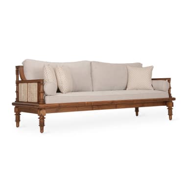 A three-seater sofa featuring a robust exposed wooden frame with a natural finish, intricate woven cane panels on the armrests, and turned legs. It is upholstered with thick, light beige fabric seat and back cushions, accompanied by two matching bolster pillows and two patterned throw pillows. — 3D model