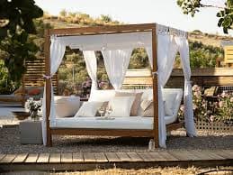 A modern outdoor canopy daybed featuring a natural light-toned wooden frame, a white fabric canopy, and matching white, thick upholstered cushions with several beige throw pillows. — 3D model