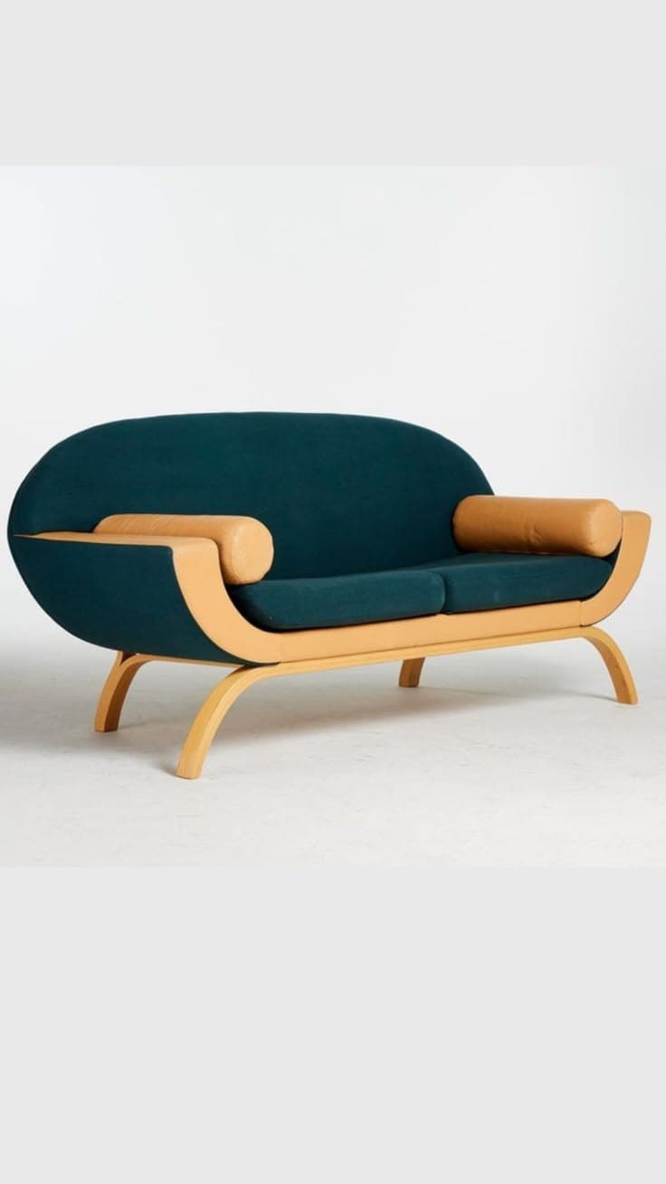 A contemporary loveseat featuring a gracefully curved bentwood frame with dark teal fabric upholstery and tan cylindrical bolster pillows. The frame wraps around the back and sides, creating an integrated shell. — 3D model