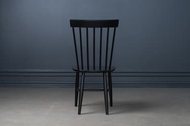 A classic black lacquered Windsor-style dining chair, featuring a tall spindle backrest and a solid wood saddle-shaped seat. The chair stands on four splayed and tapered legs, reinforced by H-stretchers, offering a timeless and sturdy design. — 3D model