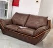 A modern two-seater sofa, upholstered in brown leather, featuring a distinct exposed wooden frame that forms the base and extends up the sides and back. The sofa has two plush seat cushions and two back cushions, all with white contrast stitching. The armrests are integrated into the overall sloped design, creating a sleek and contemporary silhouette. The piece is elevated slightly on small, recessed feet. — 3D model