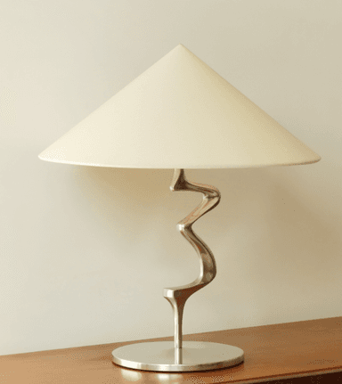 A modern table lamp featuring a distinctive serpentine metal stem, a circular base, and a conical fabric shade. The design emphasizes sculptural form and a polished finish. — 3D model