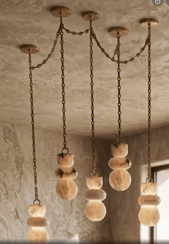 A sophisticated multi-pendant chandelier featuring five individual light drops. Each drop is suspended by a brass chain from a small, circular brass ceiling canopy. These canopies are interconnected by additional brass chains, creating a linear arrangement. The light diffusers are crafted from translucent, veined stone, likely onyx or alabaster, shaped into organic, stacked forms that illuminate to reveal their natural patterns. — 3D model