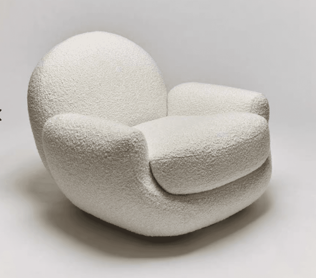 A plush, contemporary lounge chair upholstered in a textured, off-white bouclé fabric, featuring a rounded, organic silhouette. The chair has a low profile with no visible legs, consisting of a continuous, fully upholstered form that includes the backrest, seat, and wide, integrated armrests. Its design emphasizes comfort and a soft, inviting aesthetic. — 3D model