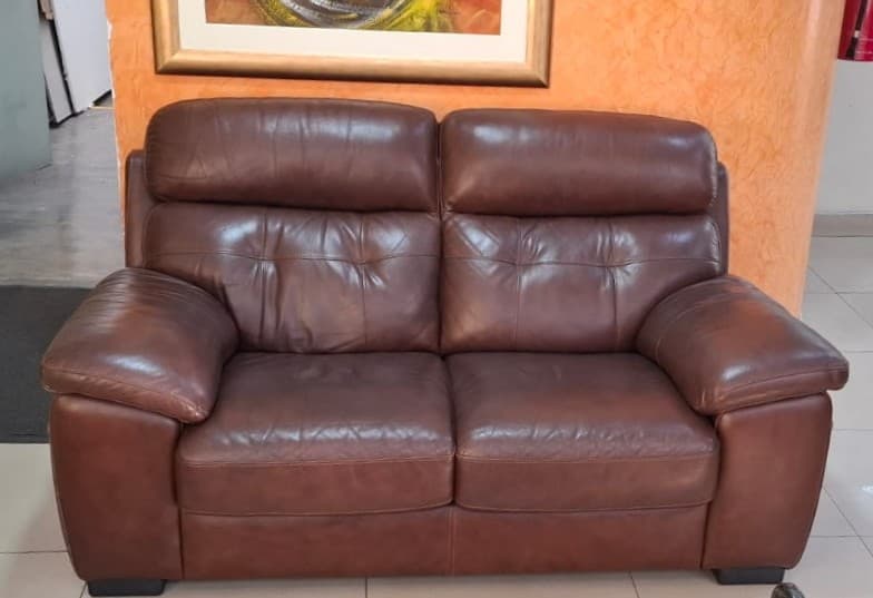 A contemporary two-seater loveseat upholstered in rich brown leather. It features plump, padded seat and back cushions with integrated headrests, along with wide, rounded track arms. The loveseat rests on short, dark, rectangular block feet. — 3D model