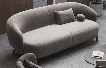 A modern, rounded loveseat with a soft, organic silhouette, upholstered in a light beige fabric. It features a continuous, curved back and armrest design, an integrated seat cushion, and is supported by slender black metal legs. Two loose accent pillows, one rectangular and one spherical, accompany the loveseat. — 3D model