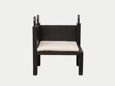 A high-backed armchair characterized by its robust, block-like construction and dark, roughly textured wood. The chair features broad, integrated armrests and a tall backrest topped with three distinct, carved finials. A simple, thin white seat cushion with a black piped edge provides seating contrast. — 3D model