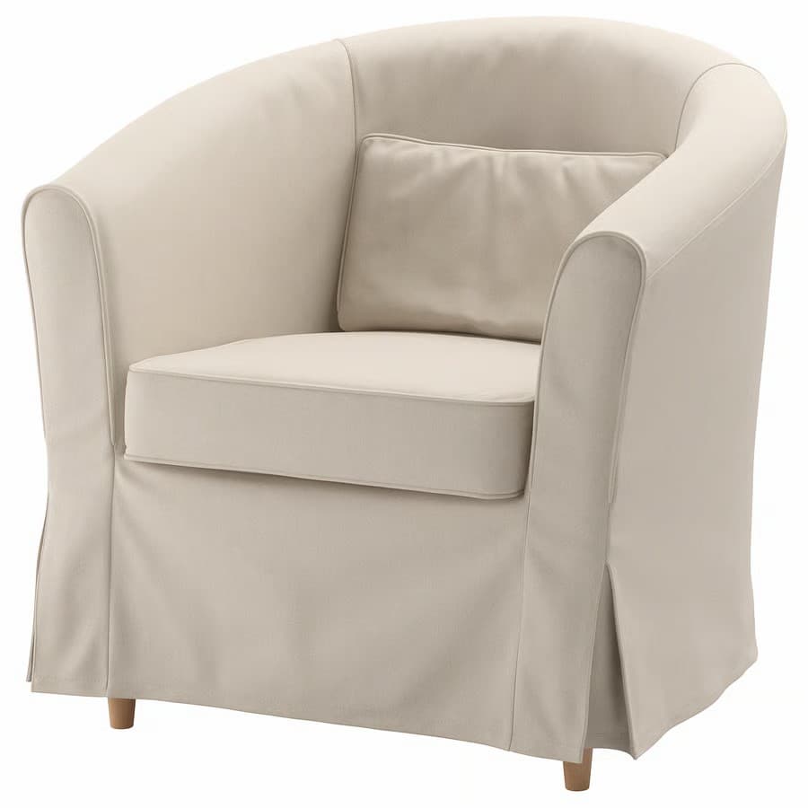 A light-colored armchair with a rounded back and arms, upholstered in fabric. It features a seat cushion and a lumbar pillow. The armchair has a skirted base that extends to the floor and is supported by short, wooden legs. — 3D model