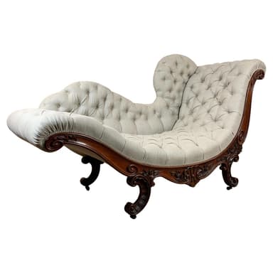 An ornate chaise lounge featuring a dark, elaborately carved wooden frame and light-colored button-tufted fabric upholstery. The design incorporates scrolled elements on the frame, armrest, and backrest, alongside cabriole legs. The asymmetrical form is designed for reclining comfort. — 3D model