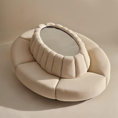 A low-profile, circular upholstered coffee table featuring a segmented padded base in a cream-colored textile. It has a raised oval-shaped central section with vertical channel tufting that houses an integrated mirrored surface. — 3D model