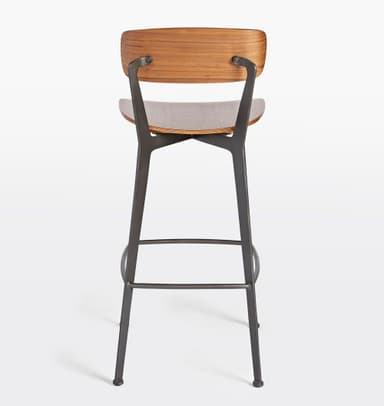 A bar stool with a backrest, featuring a wooden seat and back panel, supported by a dark metal frame. The seat and back panel appear to be made of bent wood or plywood with a wood grain finish. The frame consists of angled legs connected by a footrest at the bottom and supports for the seat and back. The design is modern and minimalist. — 3D model