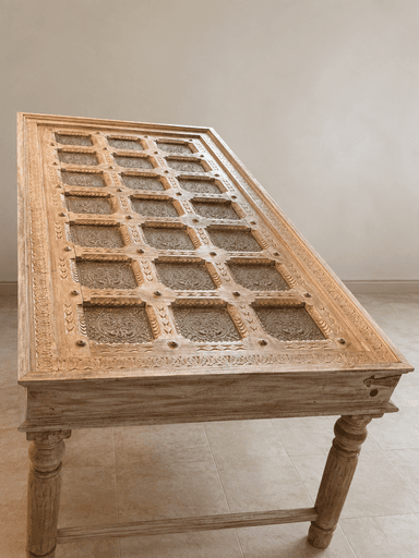 A rectangular coffee table crafted from light-toned wood, featuring extensively carved details on its frame and legs. The tabletop is segmented into a grid pattern, with each square section containing an ornate metal grille insert. The table stands on four turned legs connected by a stretcher bar, exhibiting a traditional or ethnic design aesthetic. — 3D model