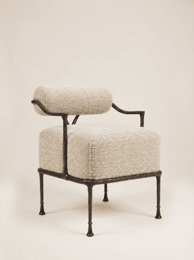 An accent chair featuring a dark, hammered or forged metal frame and upholstered in a light-colored, textured boucle-like fabric. The design includes a separate cylindrical bolster for the backrest and a rectangular cushion for the seat. The metal frame forms minimal armrests and sturdy, tapered legs with small feet. The overall aesthetic is modern and artisanal. — 3D model