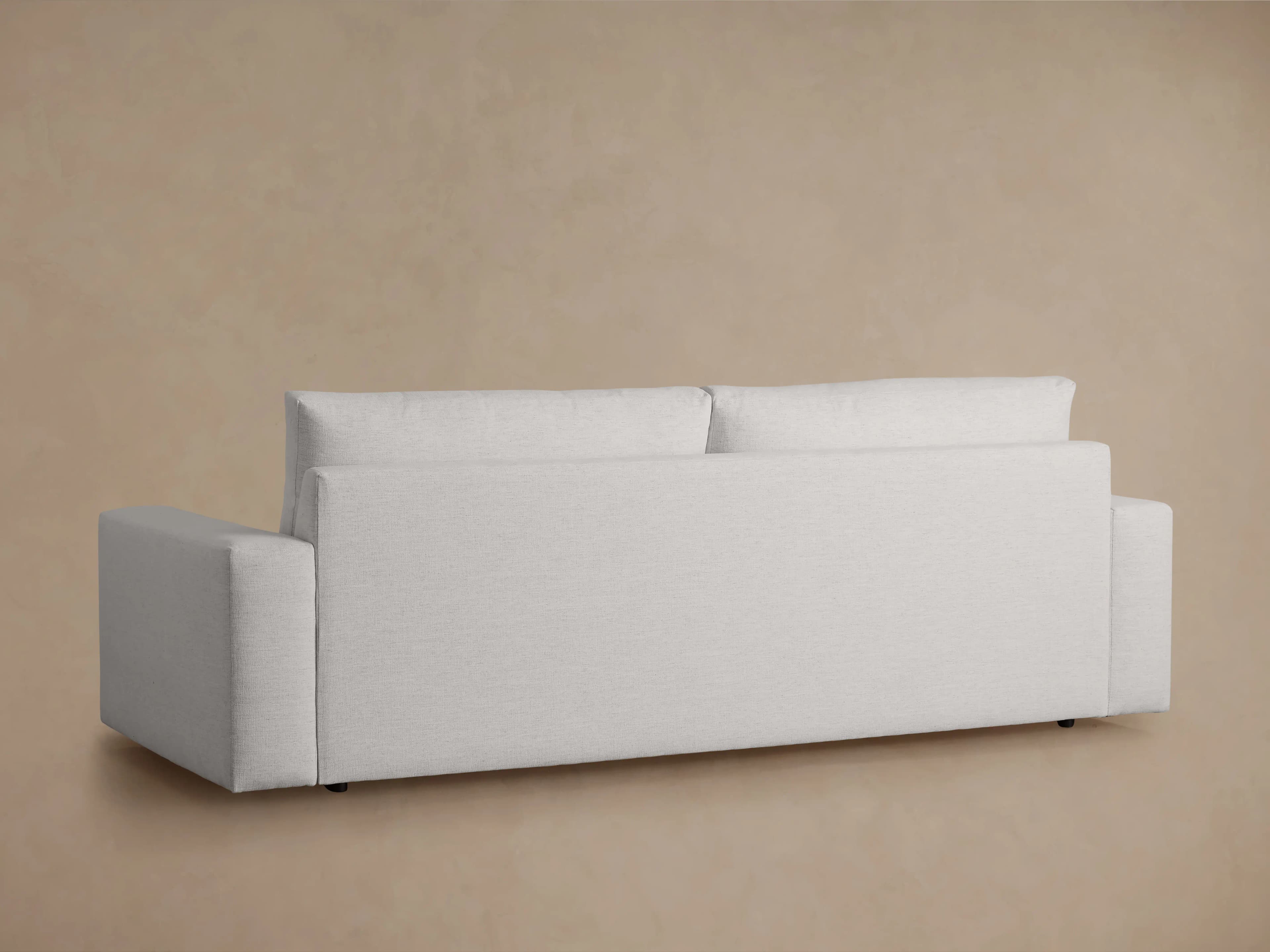 A modern, upholstered sofa viewed from the back. It features clean lines, square arms, and a relatively low profile. The upholstery appears to be a textured fabric in a light color. The sofa has two distinct back cushions and an extended base. — 3D model