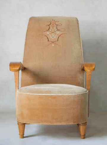 A vintage armchair with a high back and upholstered in a light brown, velvety fabric. The armrests are made of polished wood, featuring a curved design. The legs are also wooden, with decorative turned details on the front legs and a more modern, angled design on the back legs. — 3D model