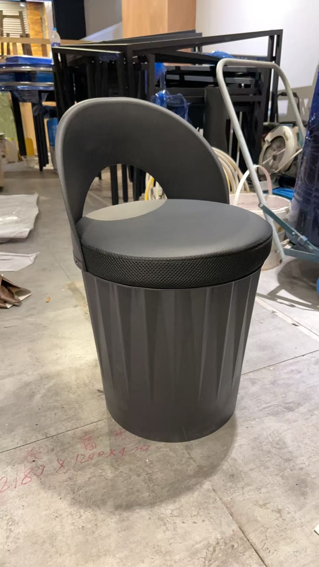A modern, monochromatic dark gray stool featuring a cylindrical base with vertical fluting and a rounded backrest. The seat is cushioned and upholstered in a contrasting textured fabric, likely for grip. The backrest is low, curved, and incorporates a cut-out design that serves as a handle. The stool is designed for compact, functional seating with a contemporary aesthetic. — 3D model