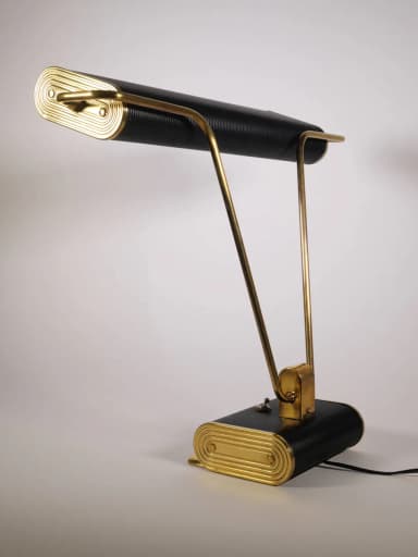 A stylish mid-century industrial desk lamp featuring a horizontal, rectangular, ribbed black shade and a matching ribbed black rectangular base. It is supported by two V-shaped polished brass arms that connect the shade to the base, with a central brass accent bracket. — 3D model